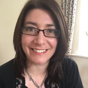 Claire Broad, a smiling woman with glasses and a necklace.