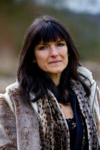 A stylish woman, Emma Restall Orr, wearing a luxurious fur coat, exuding elegance and sophistication.