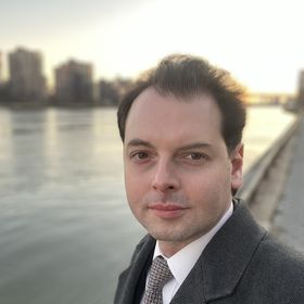 A well-dressed Jason Jorjani stands by a river, exuding professionalism and elegance.