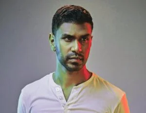 Curt Jaimungal, stands before a vibrant background, donning a white shirt.