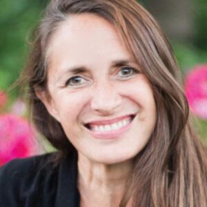 Anneke Lucas, a woman with long brown hair, radiantly smiles amidst a vibrant array of flowers.