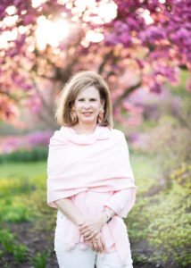 Debra Diamond is portrayed standing by a tree, adorned in a pink shawl.